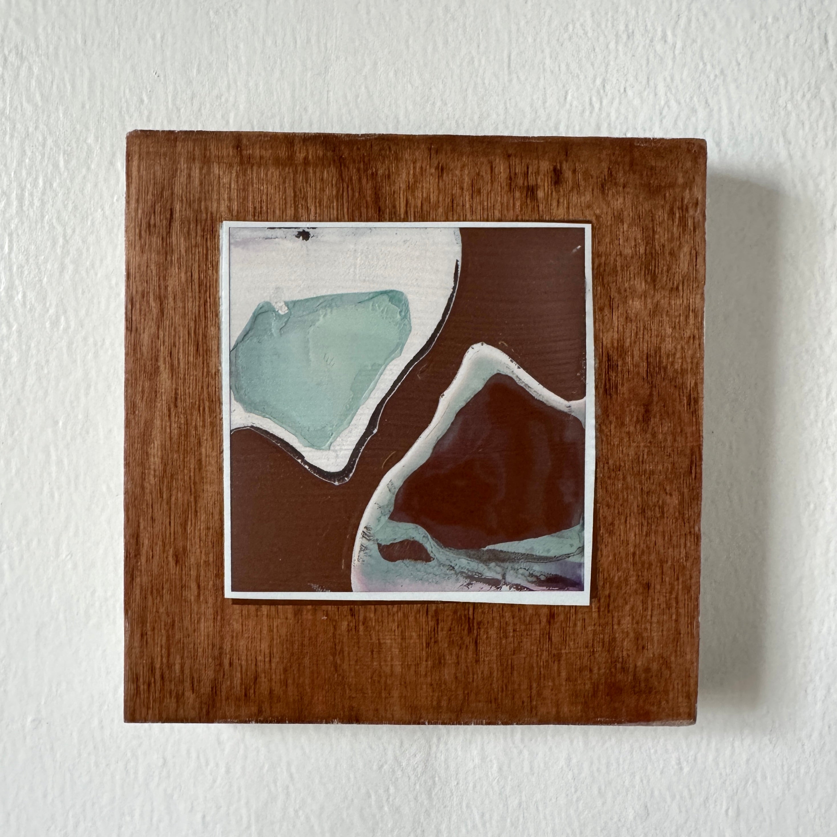 Square ceramic tile with abstract design in a wooden frame on a white wall