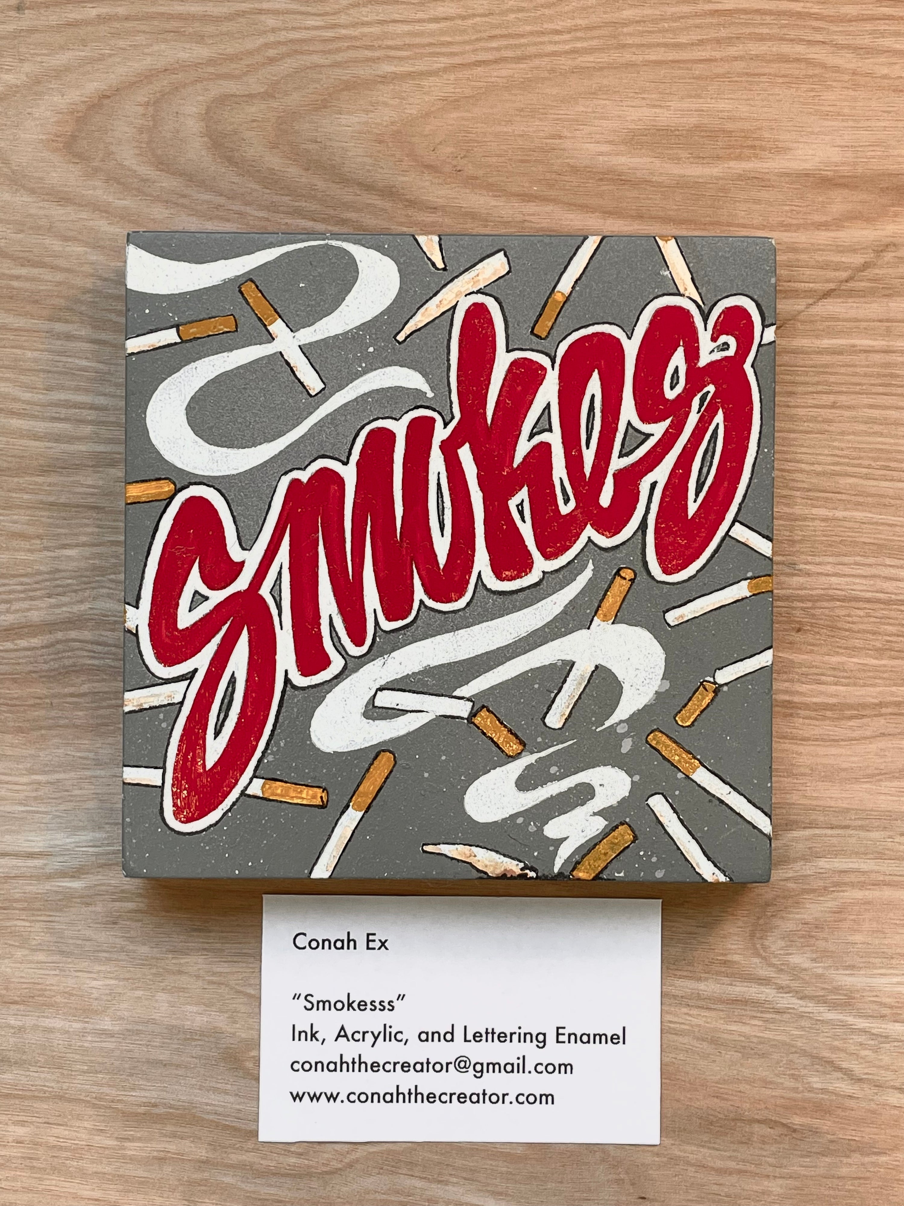 Artistic depiction of 'Smokes' with cigarette graphics on a gray background, displayed on a wooden surface.
