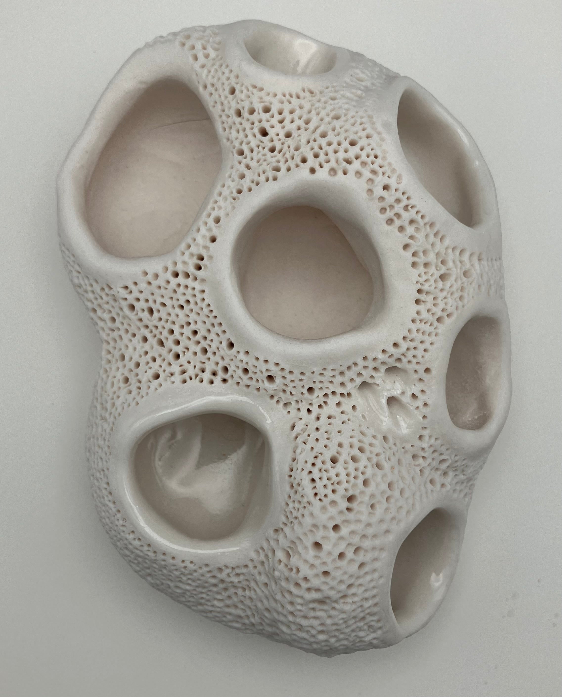 Textured ceramic vase with multiple holes on a plain background