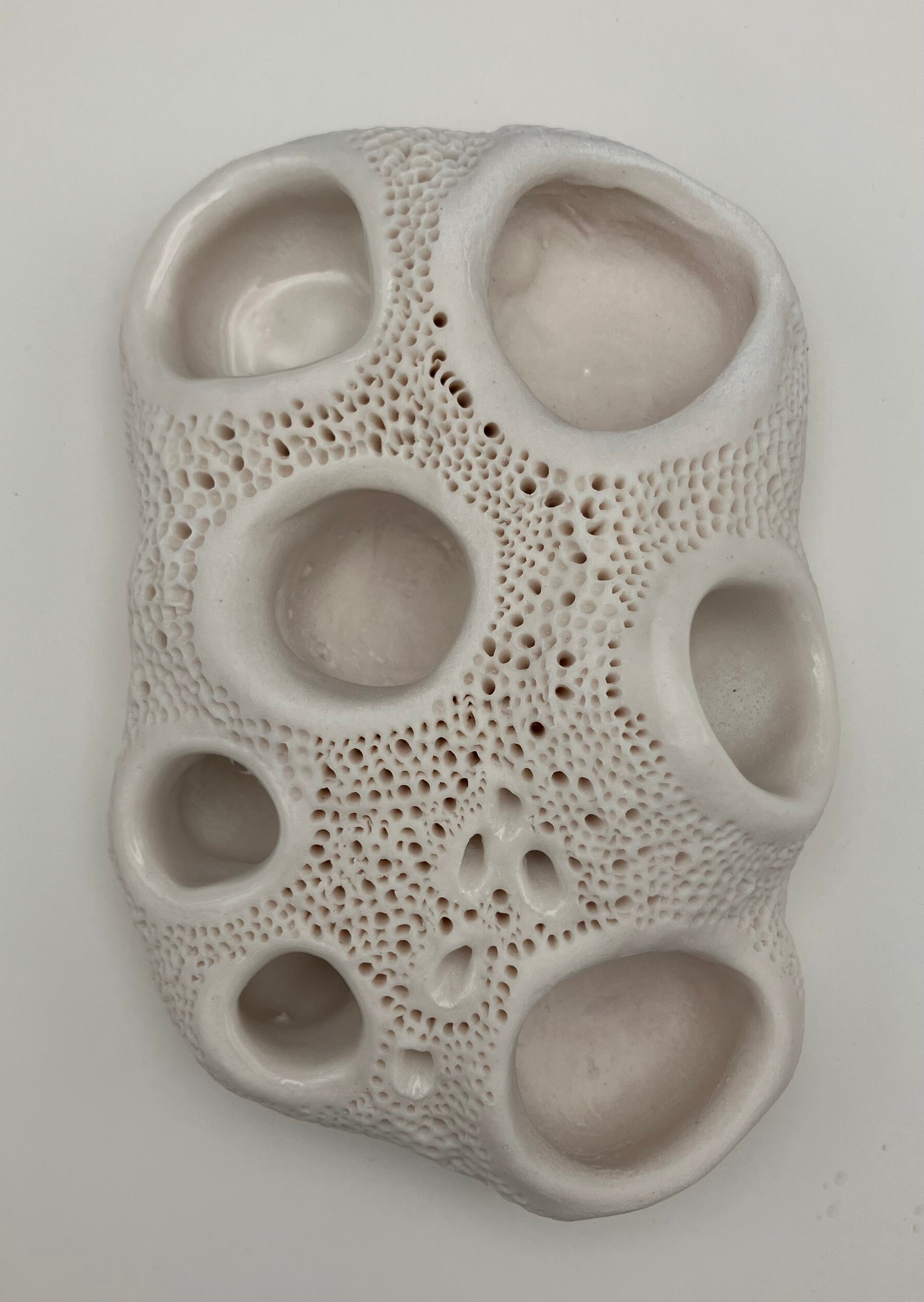 Textured ceramic wall art piece with circular holes on a white background