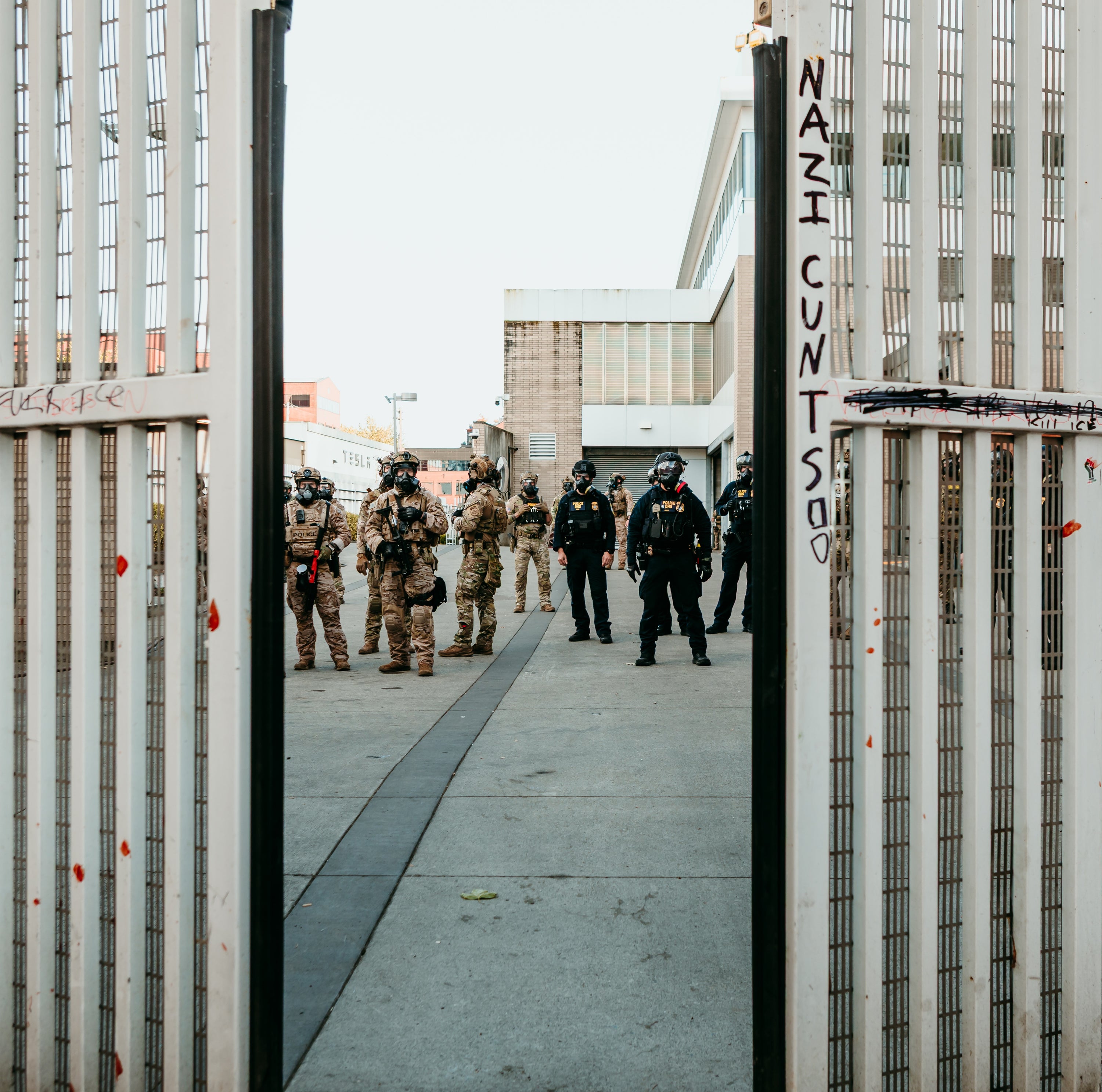 Group of people in tactical gear walking through a gate with graffiti on it.