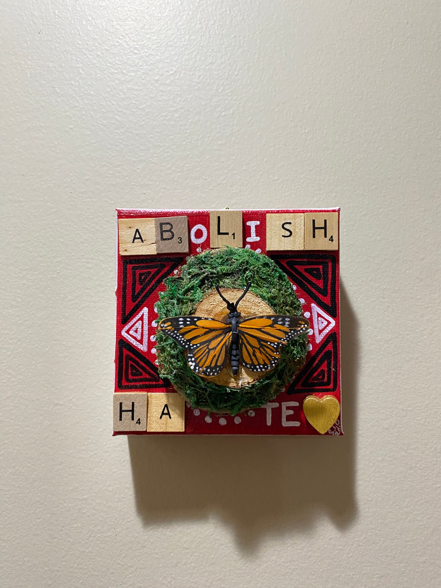 Decorative square with a butterfly, greenery, and scrabble letters spelling 'ABOLISH HAPE' on a white background.